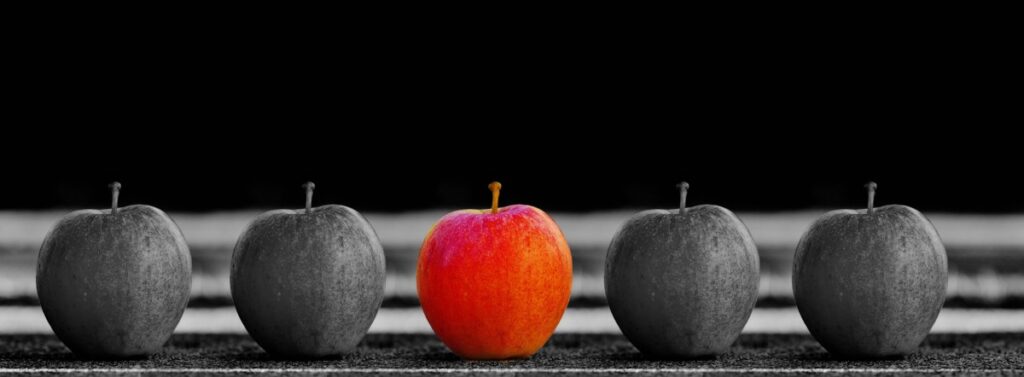 row of apples, one unique and red, the rest grayscale, signifying uniqueness