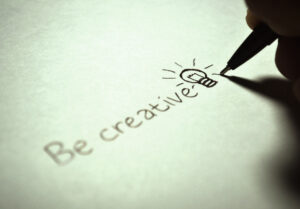 the words "be creative" being written in pen, with a light-bulb image representing creativity