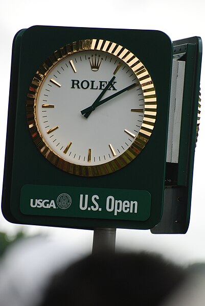 Rolex timing for the US open golf event. Gold with white face and black hands on dark green.