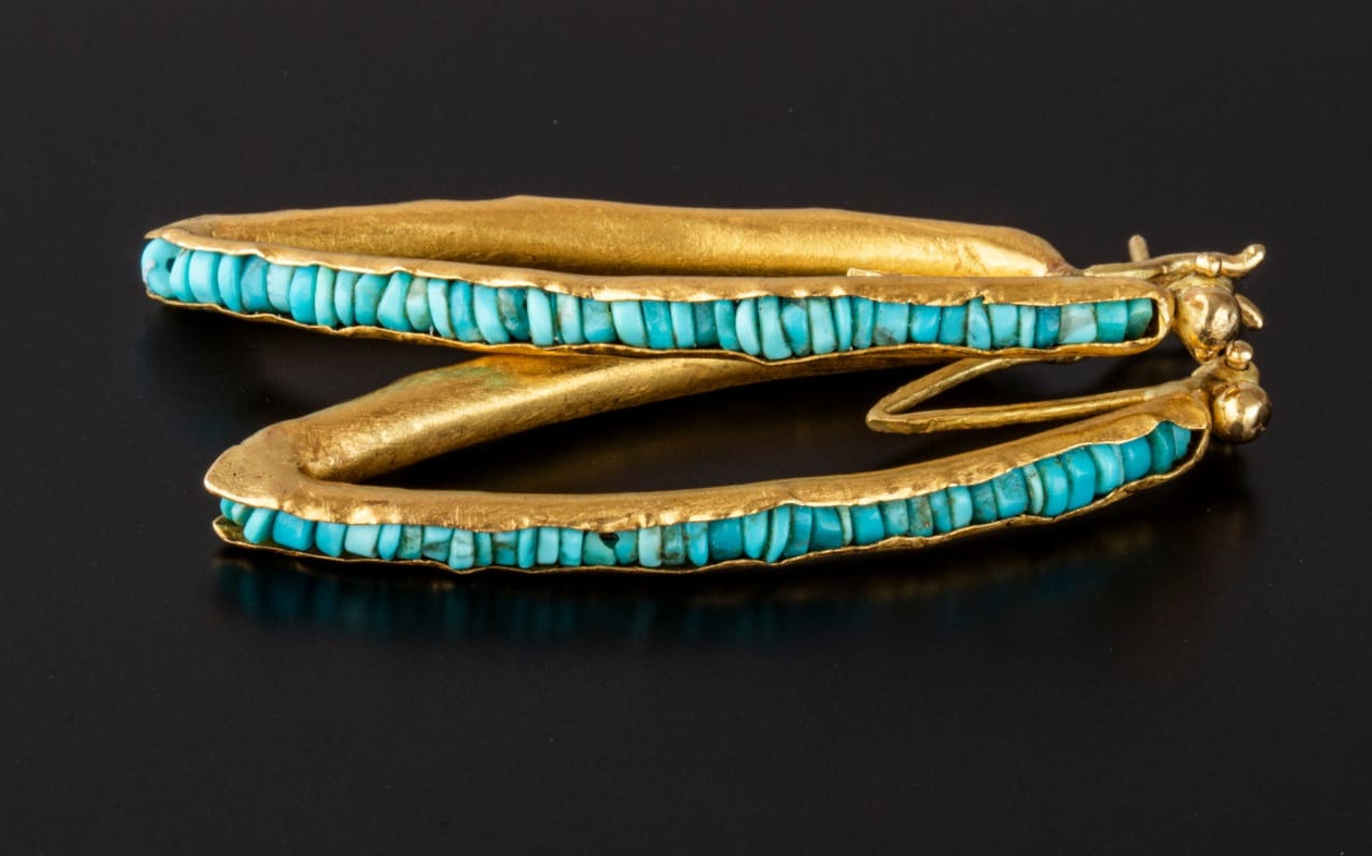 Ehud Barlev art jewellery, gold with many small turquoise stones, resting on a black surface