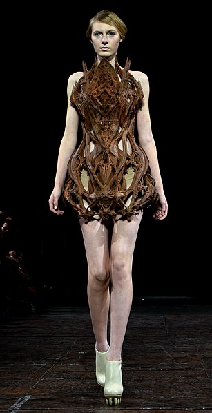 Iris van Herpen wearable art 3D printed organic brown forms, worn by a young woman, black background.