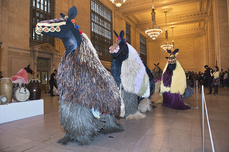 Nick Cave Soundsuits wearable art, large costumes and masks, shown inside a building.