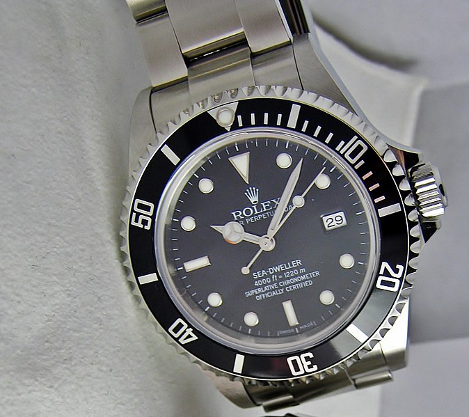 Rolex Sea Dweller diving watch, dark dial, on white fabric background.