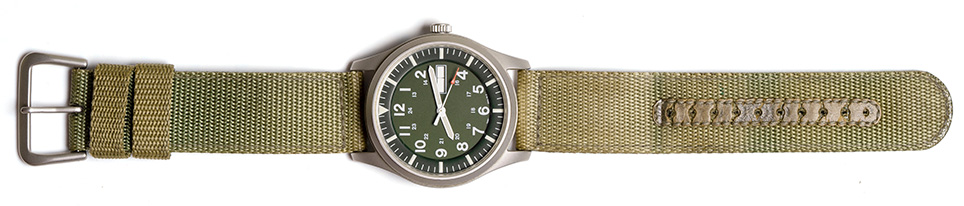 Green watch with green fabric strap, isolated on white background.