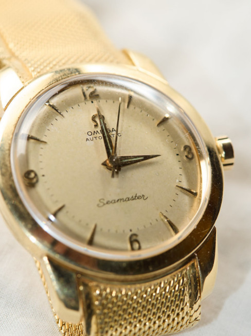 Omega Seamaster - gold watch aesthetic, gold case, dial, hands and strap, on white surface.