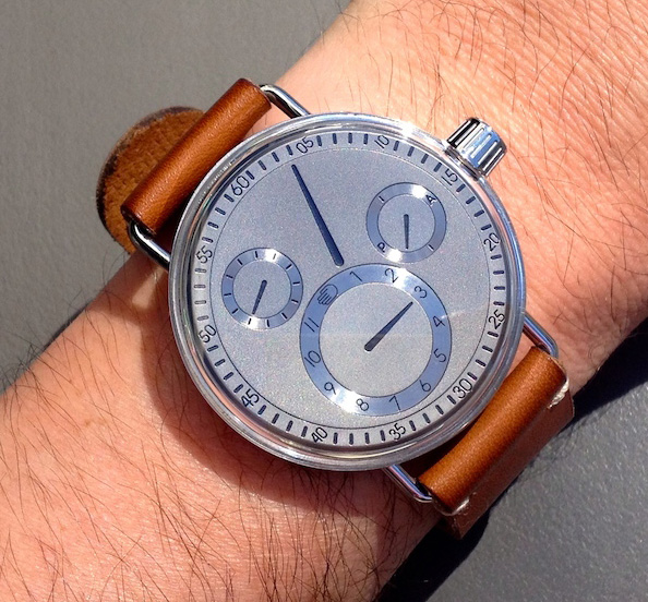 Ressence SeriesOne 1002 watch, worn on a man's wrist, grey background.