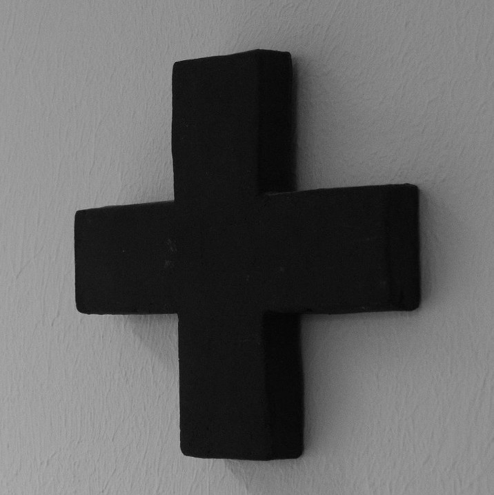 A simple wooden cross, black, on a pale wall.