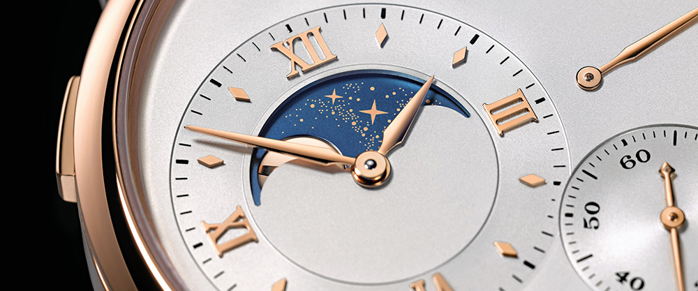 Moonphase display on a Lange-Soehne watch, closeup/detail, pale dial, gold case, black background.