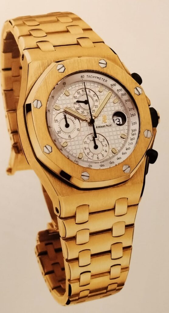 Audemars Piguet Royal Oak Cronograph watch, gold with white dial, on pale brown background.