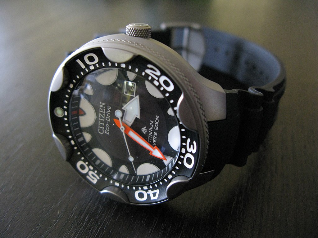 Citizen "Orca" 200m titanium watch, with a black dial and orange minute hand, on a polished wood surface.