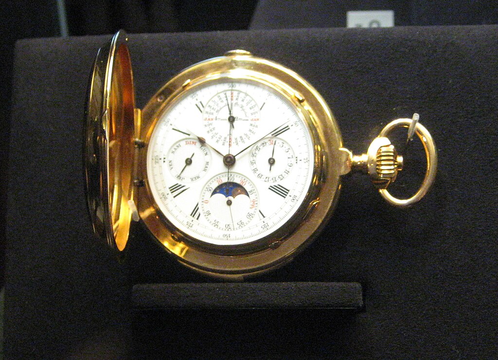 A pocket watch by Vacheron Constantin, gold with white dial and complications, on a black velvet surface.