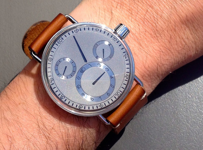 Ressence_SeriesOne watch with unusual metal dial, shown worn on a man's wrist, against a grey background.