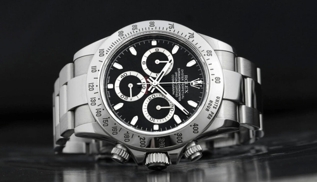 Rolex watch with black dial and complications, on a reflective surface. A black and white image.