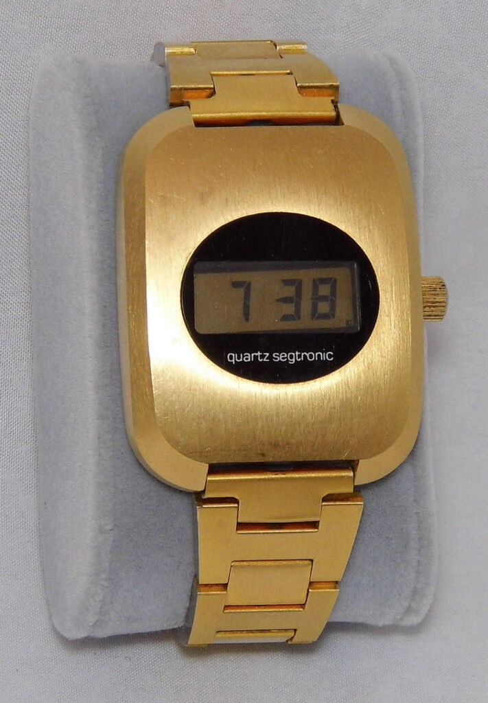 Epsa-Optel Quartz Segtronic Men's Wrist Watch, gold colour, on a grey watch-cushion and a grey fabric background.
