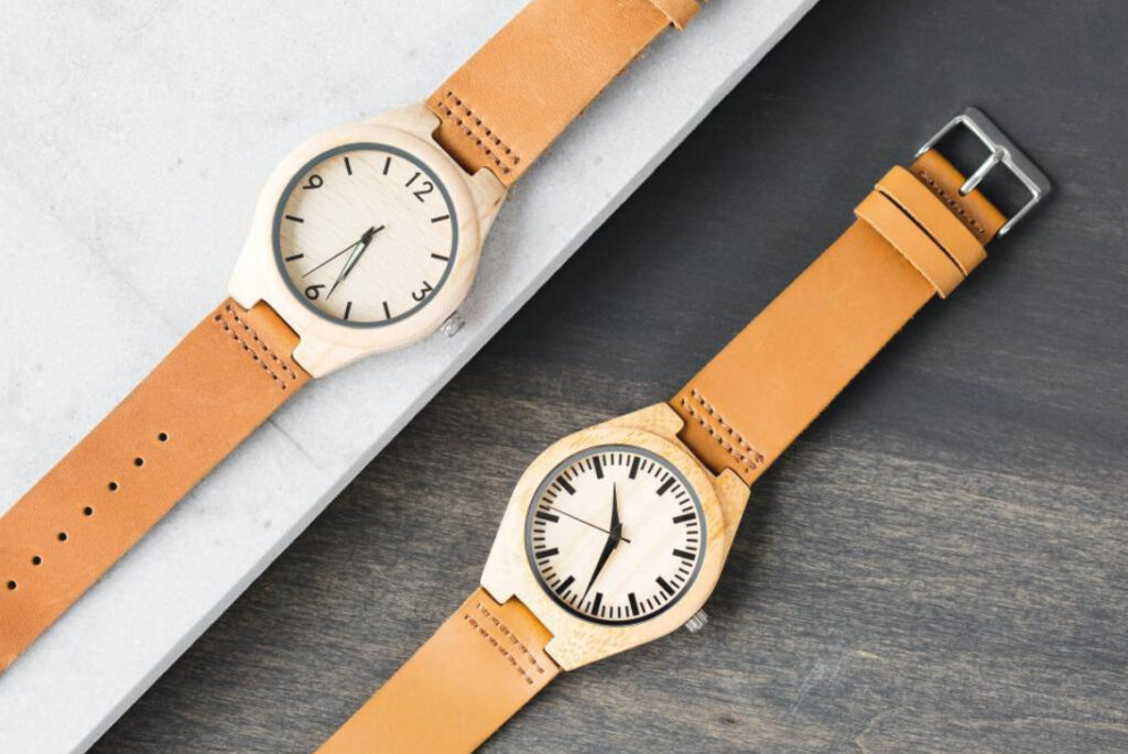2 wood watches with orange-brown leather straps, diagonally oriented. on wood and stone surfaces.
