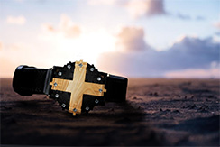Cross #1 watch in blackened silver and aspen wood, on sand with sunset
