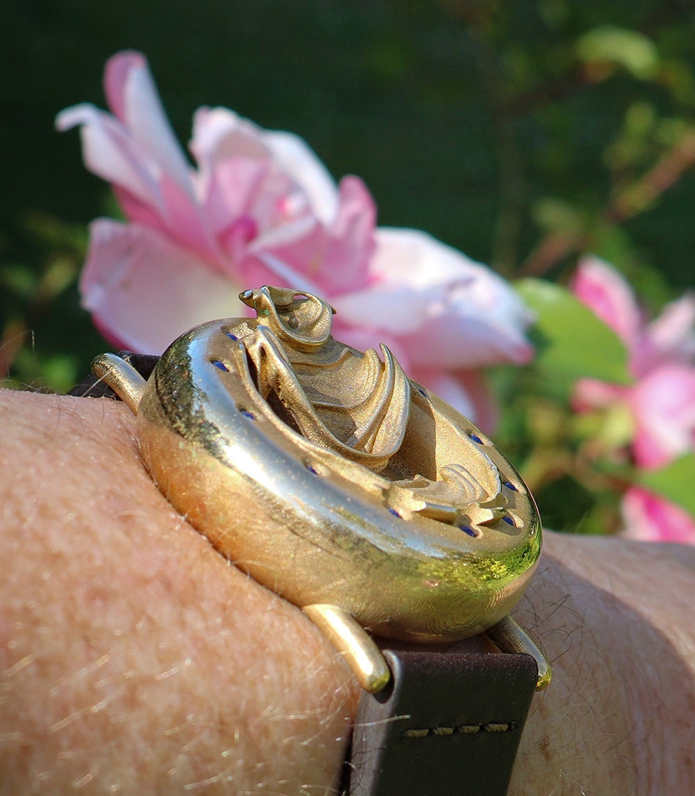 UnconstrainedTime Fractal Emergence 41mm wristwatch in bronze, on a wrist, sunlit with a rose.