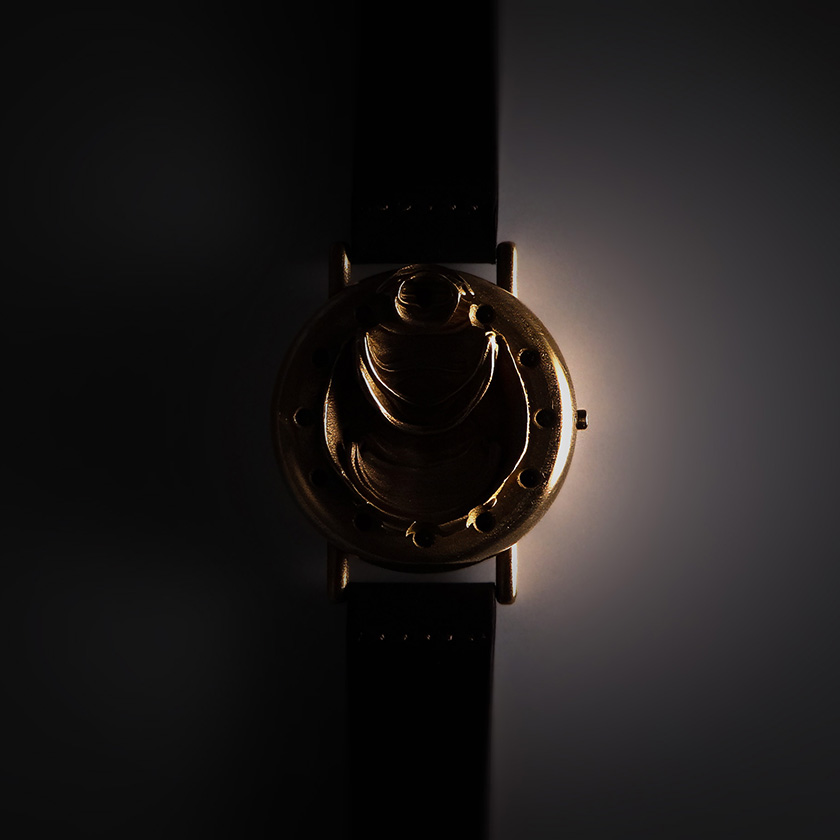 UnconstrainedTime Fractal Emergence wristwatch in bronze, on a wrist, rim-lit, with brown leather strap.