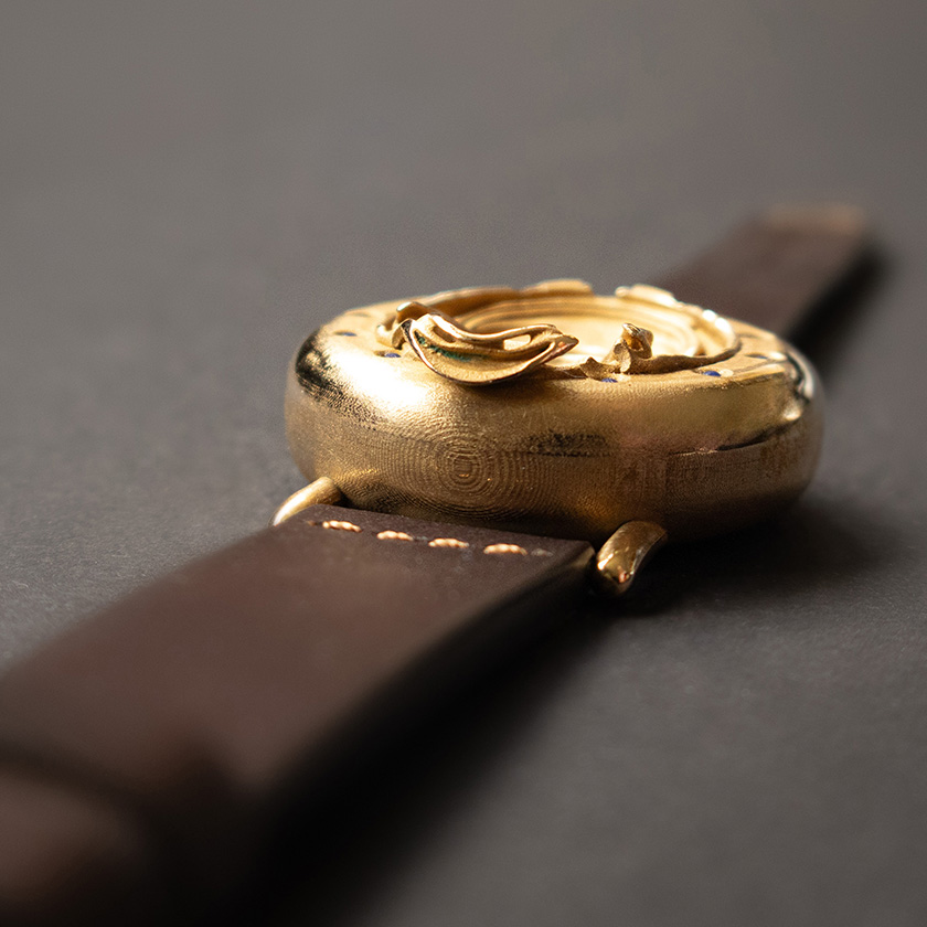 UnconstrainedTime Fractal Emergence wristwatch in bronze, end view on dark paper, with brown leather strap.