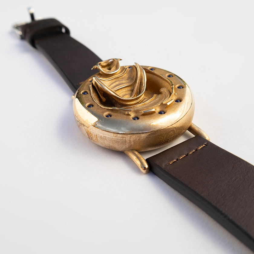 UnconstrainedTime Fractal Emergence wristwatch in bronze, angled view on white paper, with brown leather strap.